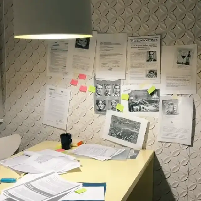 Mesa de trabajo con documentos, notas adhesivas y recortes del caso en la pared